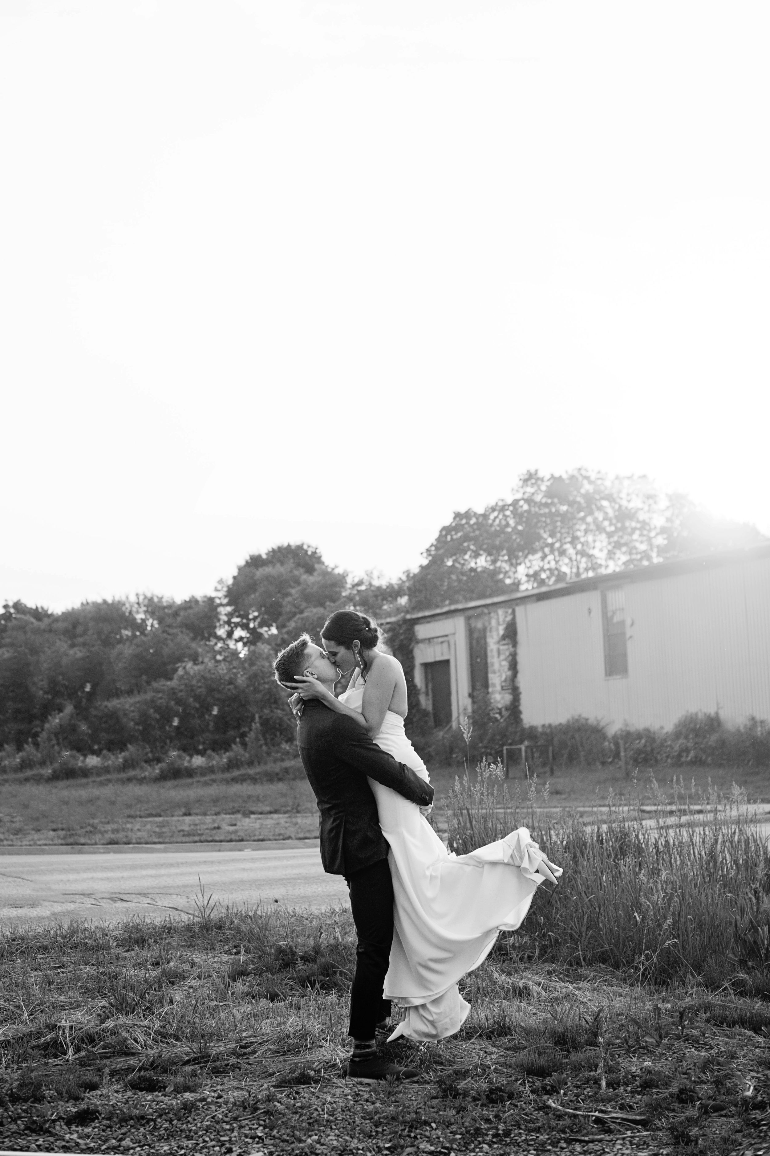 Black and white photo of groom lifting bride during romantic outdoor wedding portrait.
