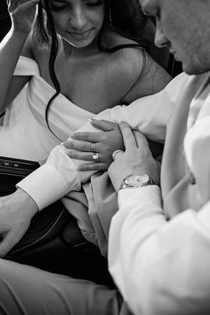 Black and white close-up of bride and groom holding hands, showcasing the wedding and engagement rings.