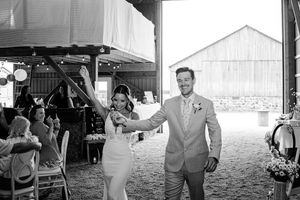 Joyful bride and groom make their grand entrance into a rustic barn wedding reception to cheering guests.