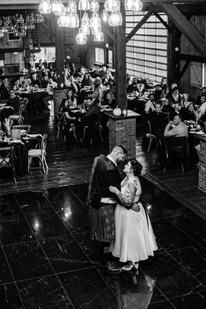 Bride and groom share first dance on shiny floor in rustic barn venue filled with guests, In Brussels Ontario.