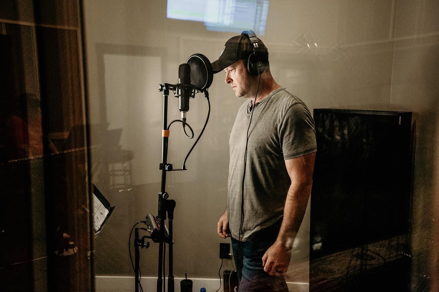 Vocalist recording in studio booth with professional microphone setup.