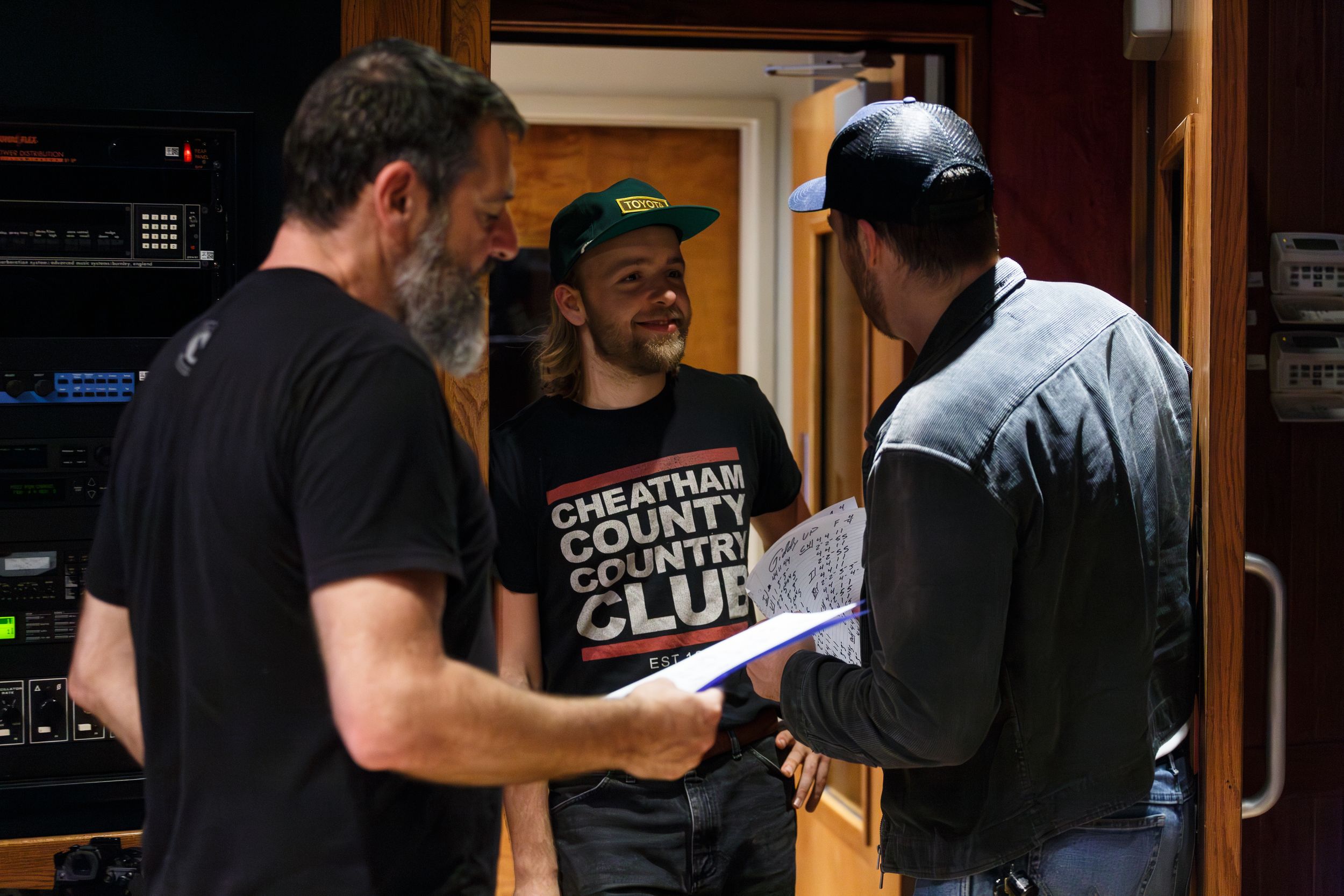 Three people discussing music charts together in recording studio environment.
