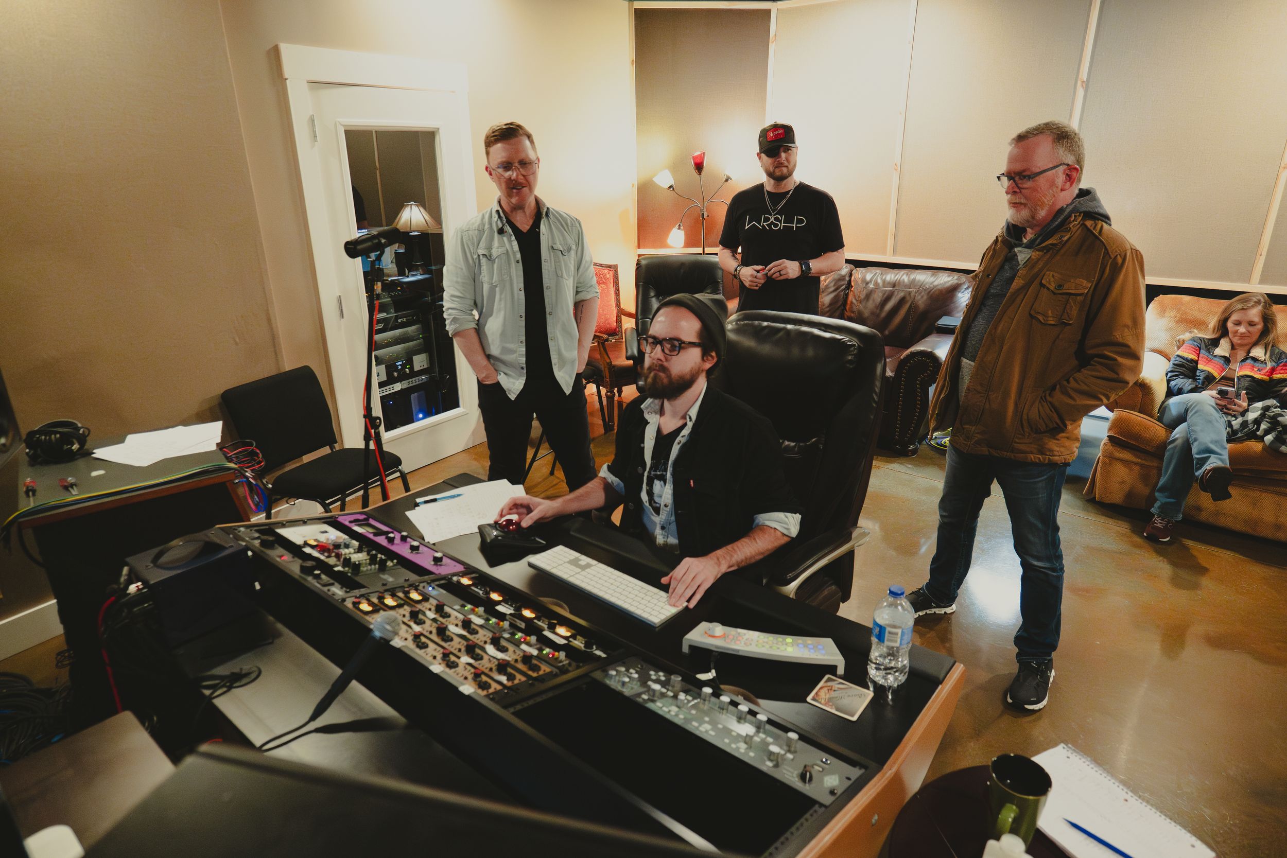 Group of musicians and producers working at mixing console in studio setting.