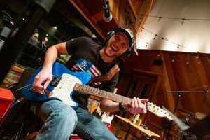 Musician playing electric guitar in recording studio with dramatic lighting.