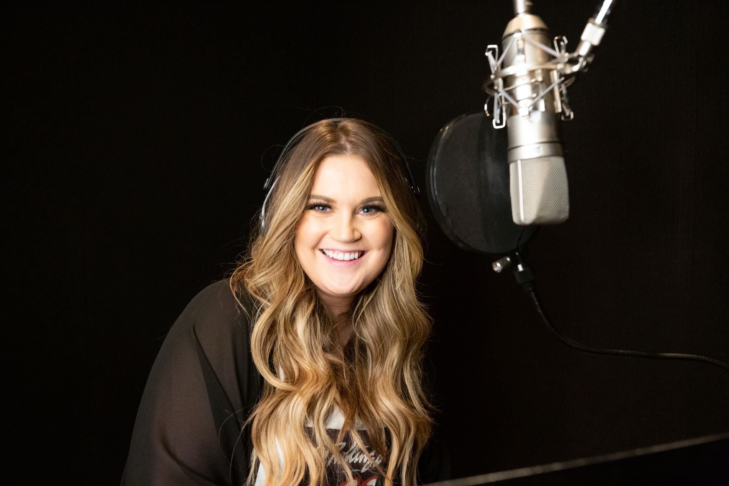 Artist smiling at microphone in recording studio with black background.