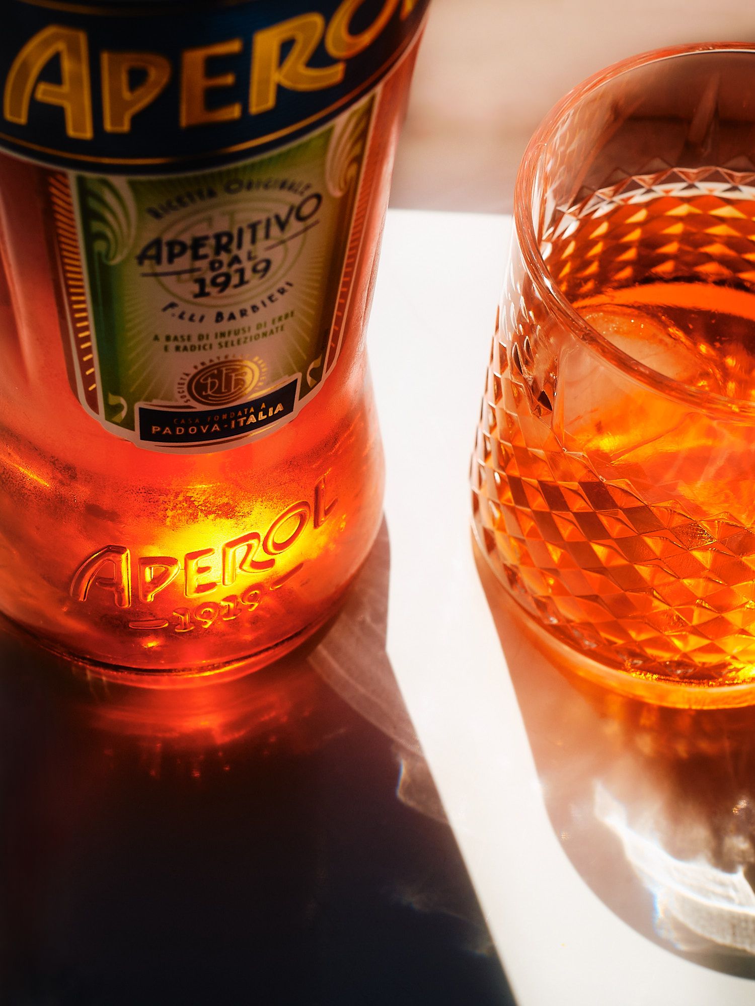 A bottle of Aperol aperitif glows orange next to a crystal glass filled with the vibrant cocktail.