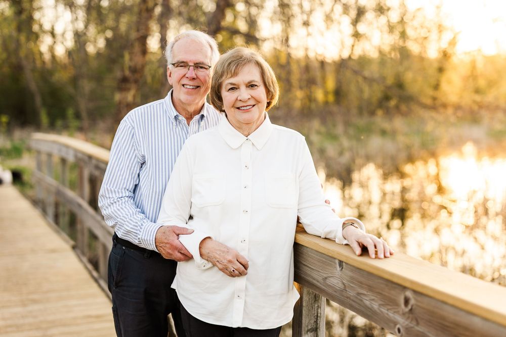 A happy couple stands on a wooden boardwalk at sunset by a tranquil lake in autumn.