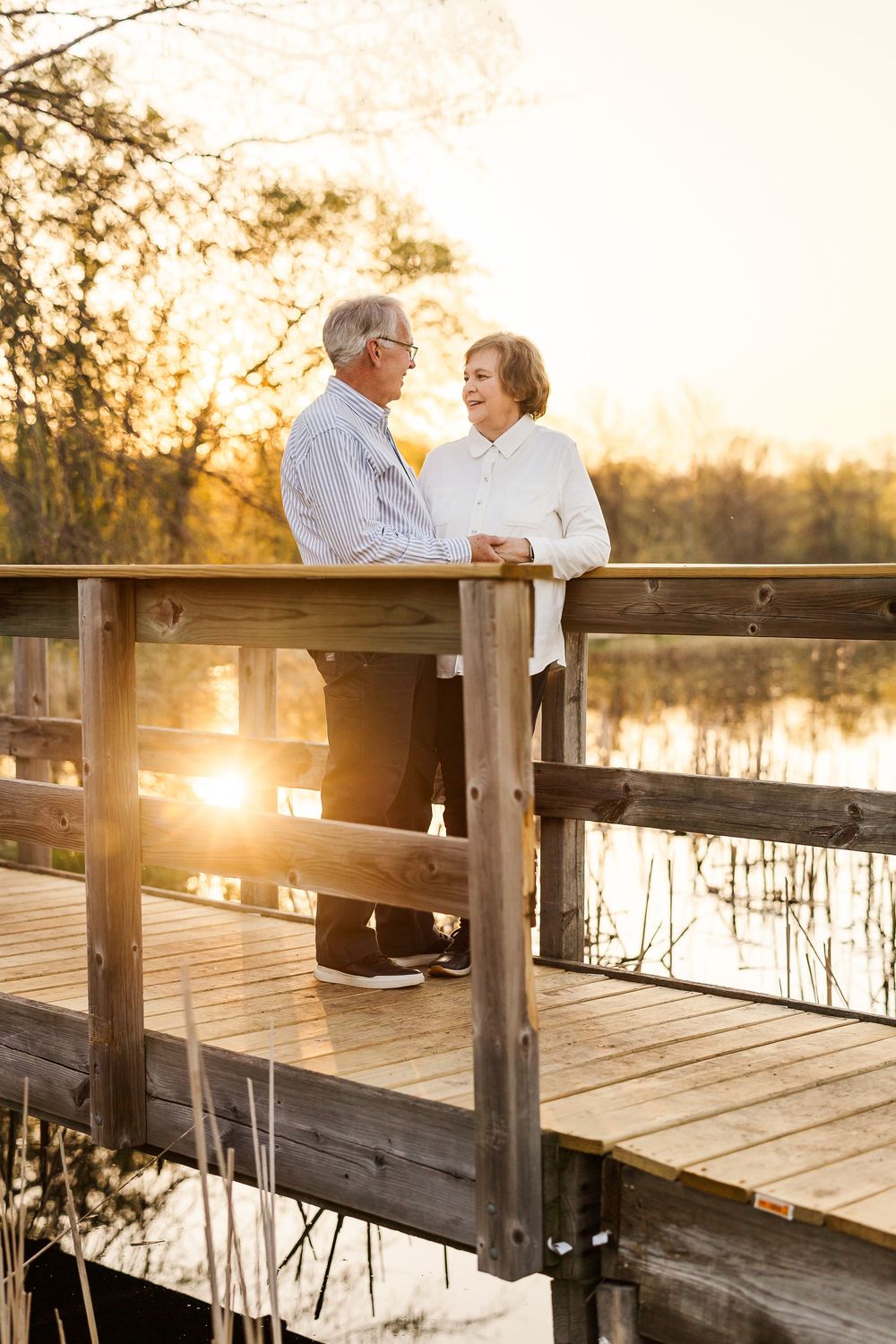 An elderly couple shares a tender moment on a wooden dock at sunset as golden light reflects off the tranquil water.