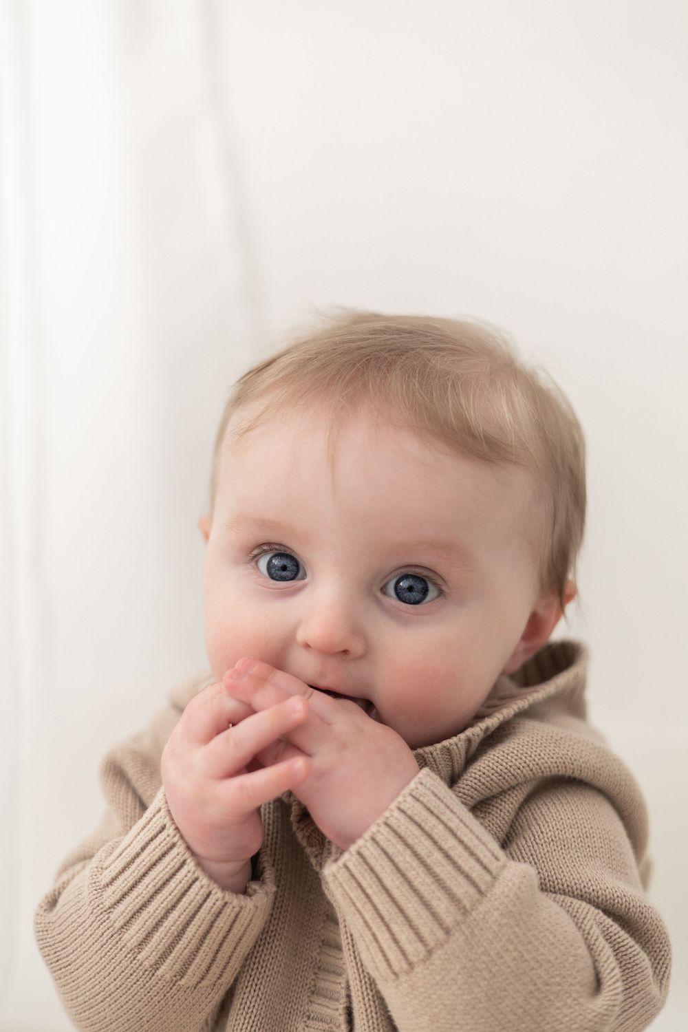 Adorable blue-eyed baby in a beige knit sweater looking curiously at the camera baby / milestone birthday photoshoot Nottingham