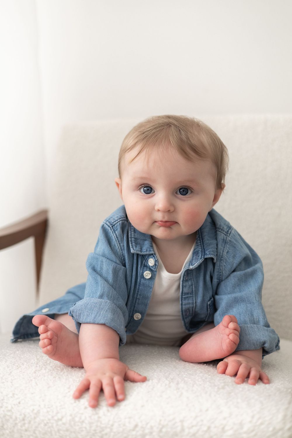 baby in denim shirt sitting upright on white fluffy surface looking at camera with bright blue eyes milestone birthday photoshoot Nottingham