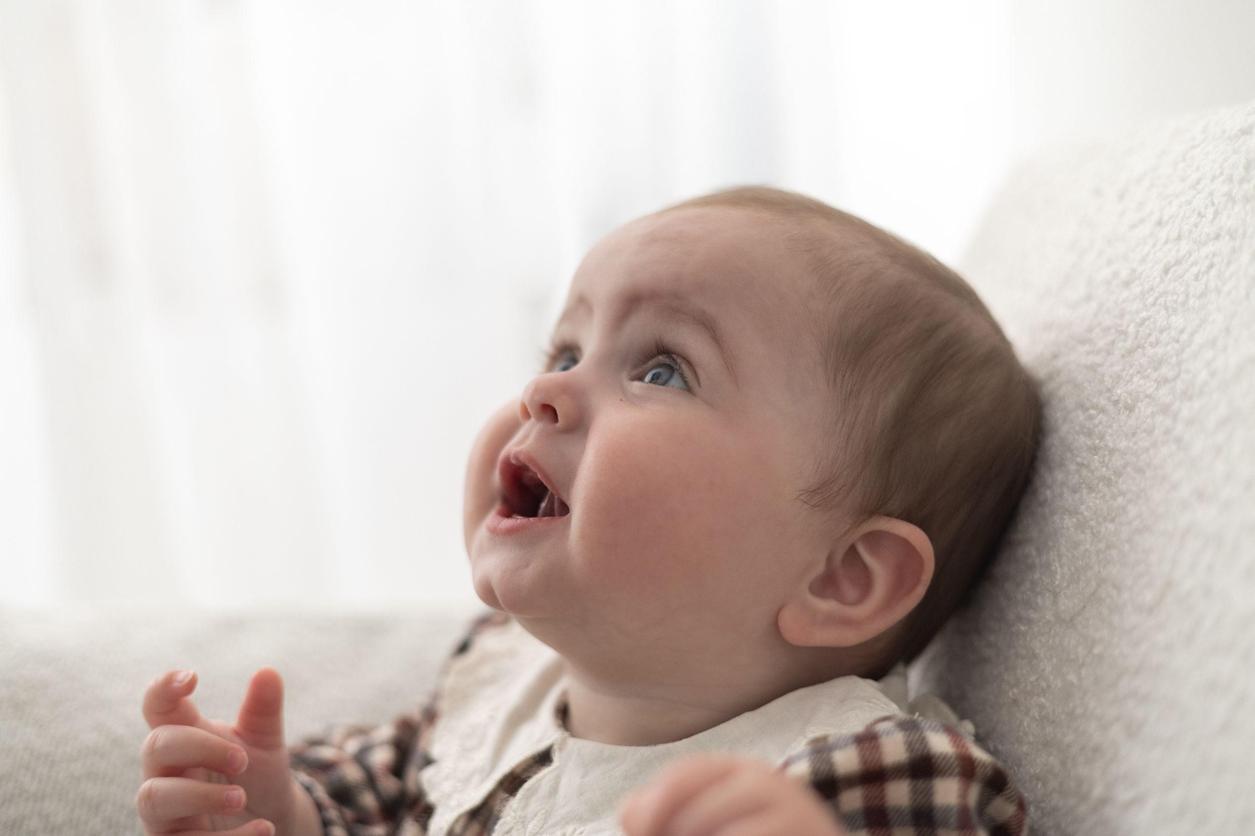 Adorable baby with blue eyes laughing and looking up while sitting on a white fluffy chair baby / milestone birthday photoshoot Nottingham