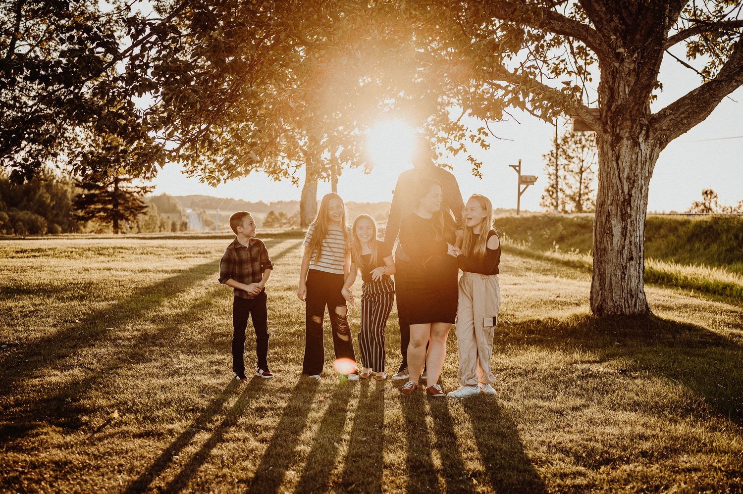 Famille en silhouette devant un coucher de soleil doré sous un grand arbre.