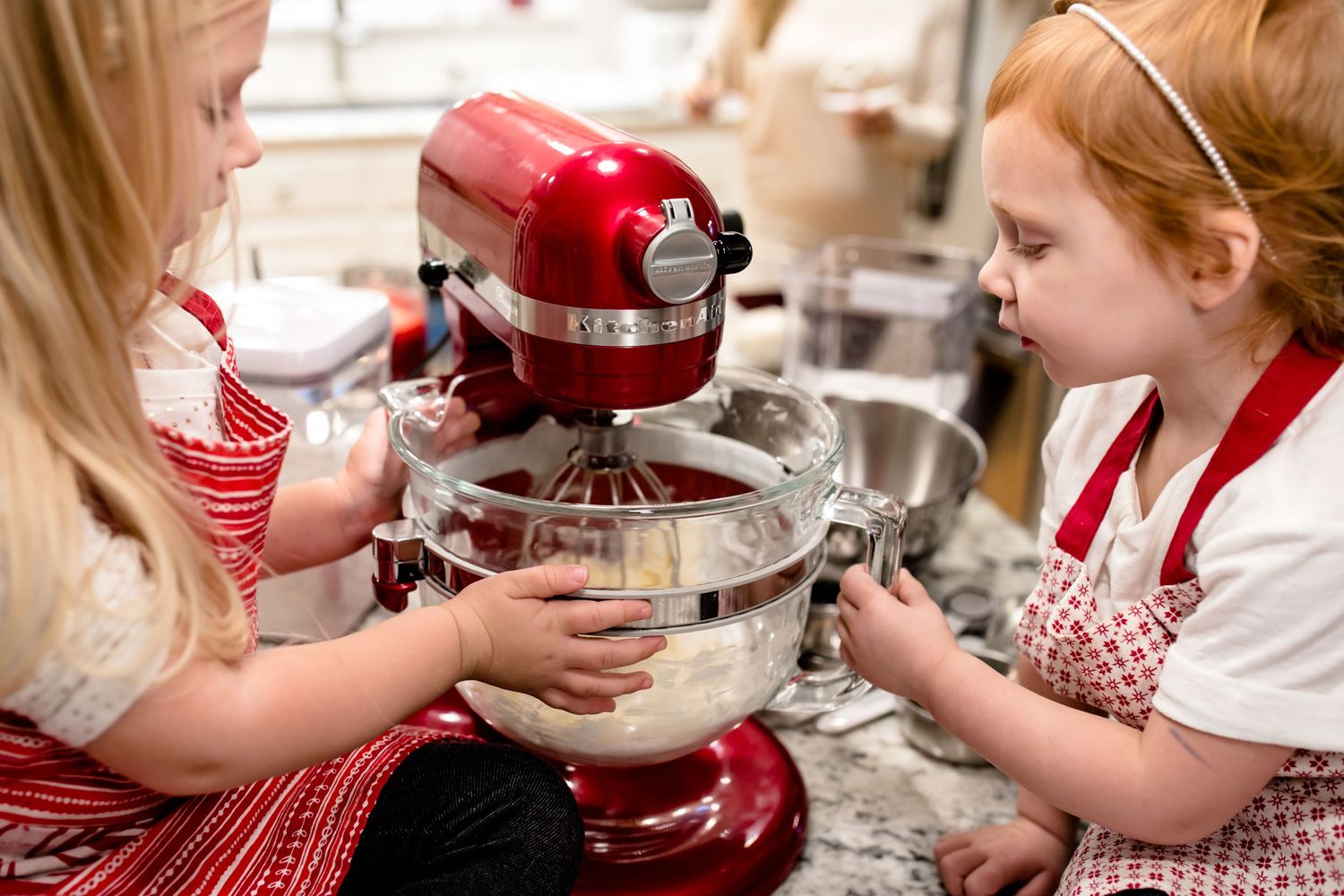 Children helping with baking using red stand mixer in kitchen.