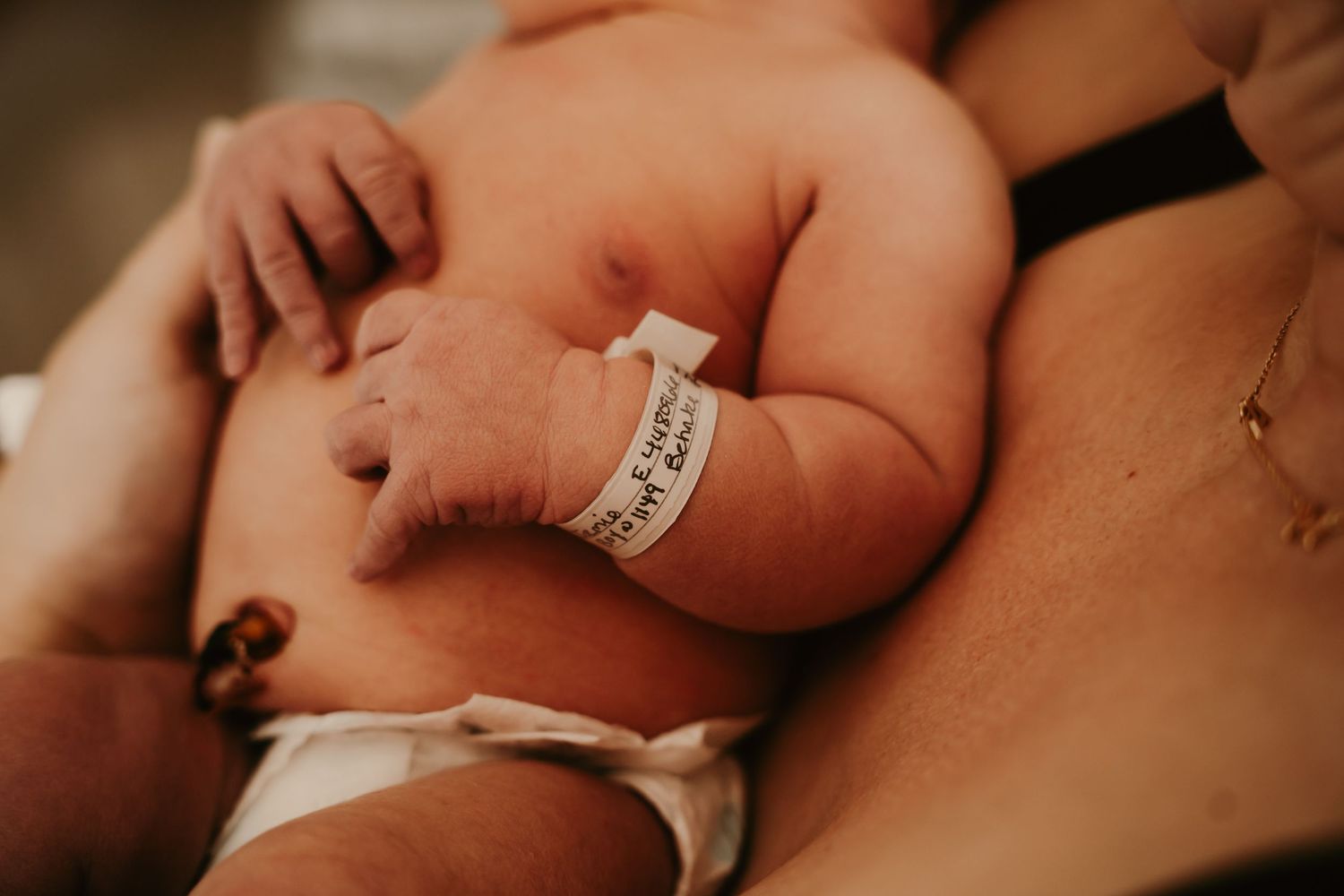 Close-up view of a newborn baby's arm with hospital identification bracelet against skin during Fresh 48 session