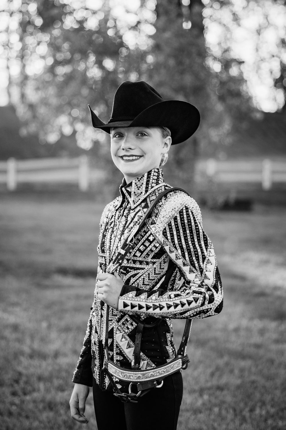 A western competitor in an ornate show jacket and cowboy hat poses outdoors.