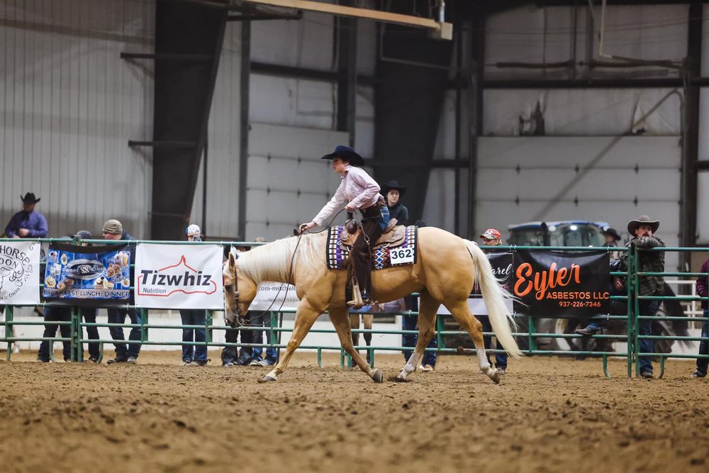 A rodeo rider performs on a palomino horse in an indoor arena.