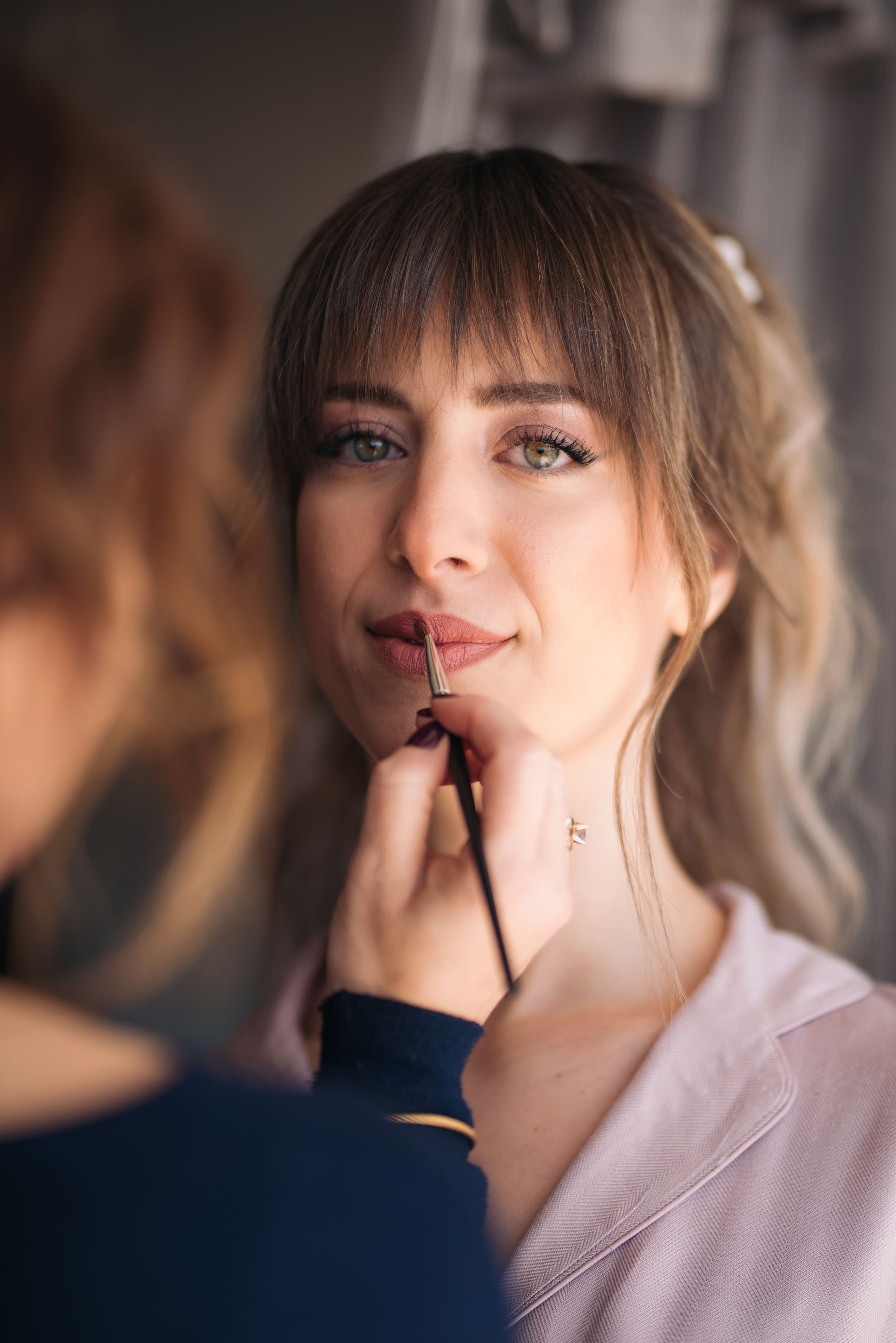 Professional makeup artist applying lip color during bridal beauty preparation.