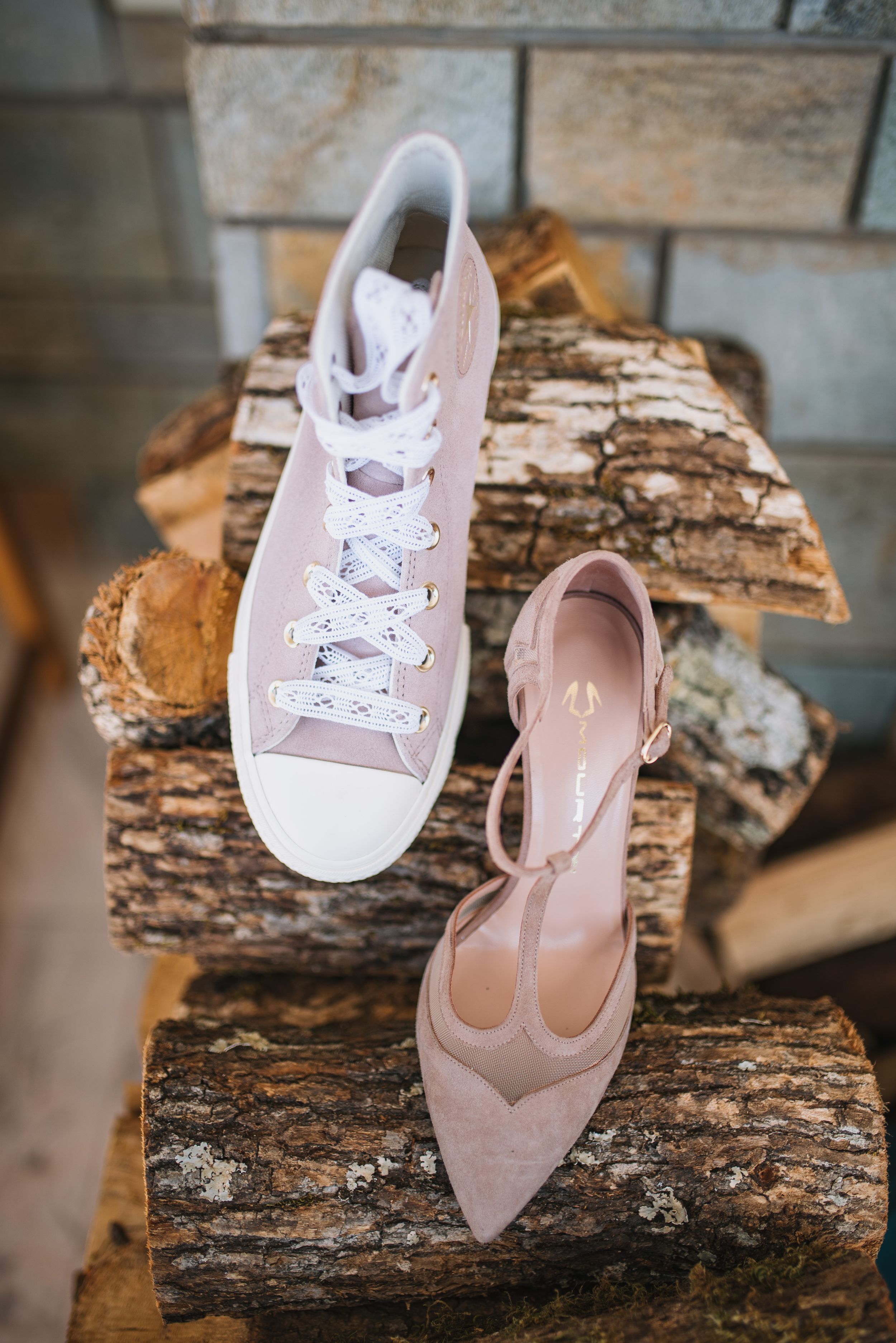 A pink Converse sneaker and matching heeled shoe displayed on rustic wood logs.