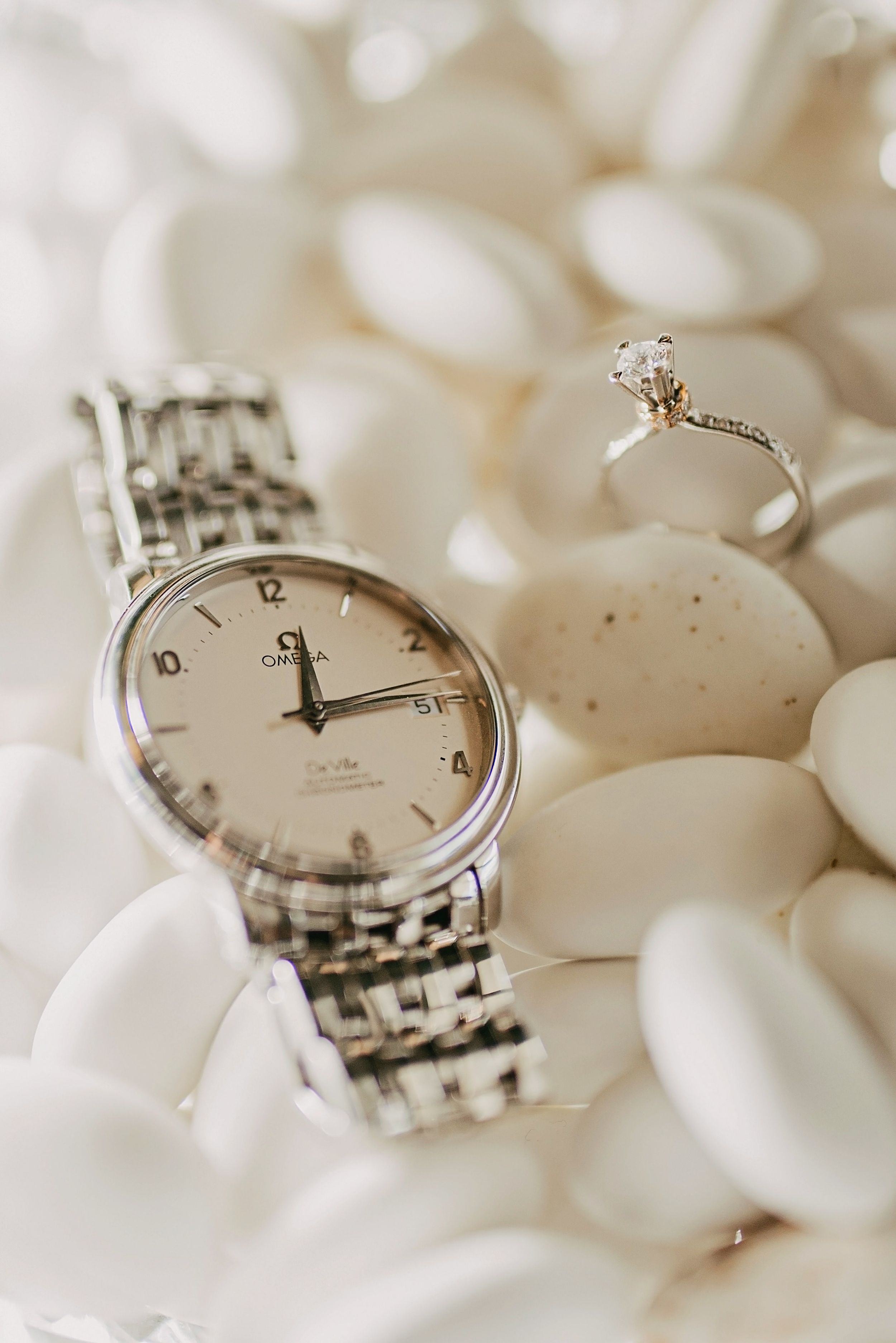 An elegant watch and diamond ring arranged on white stones in soft lighting.