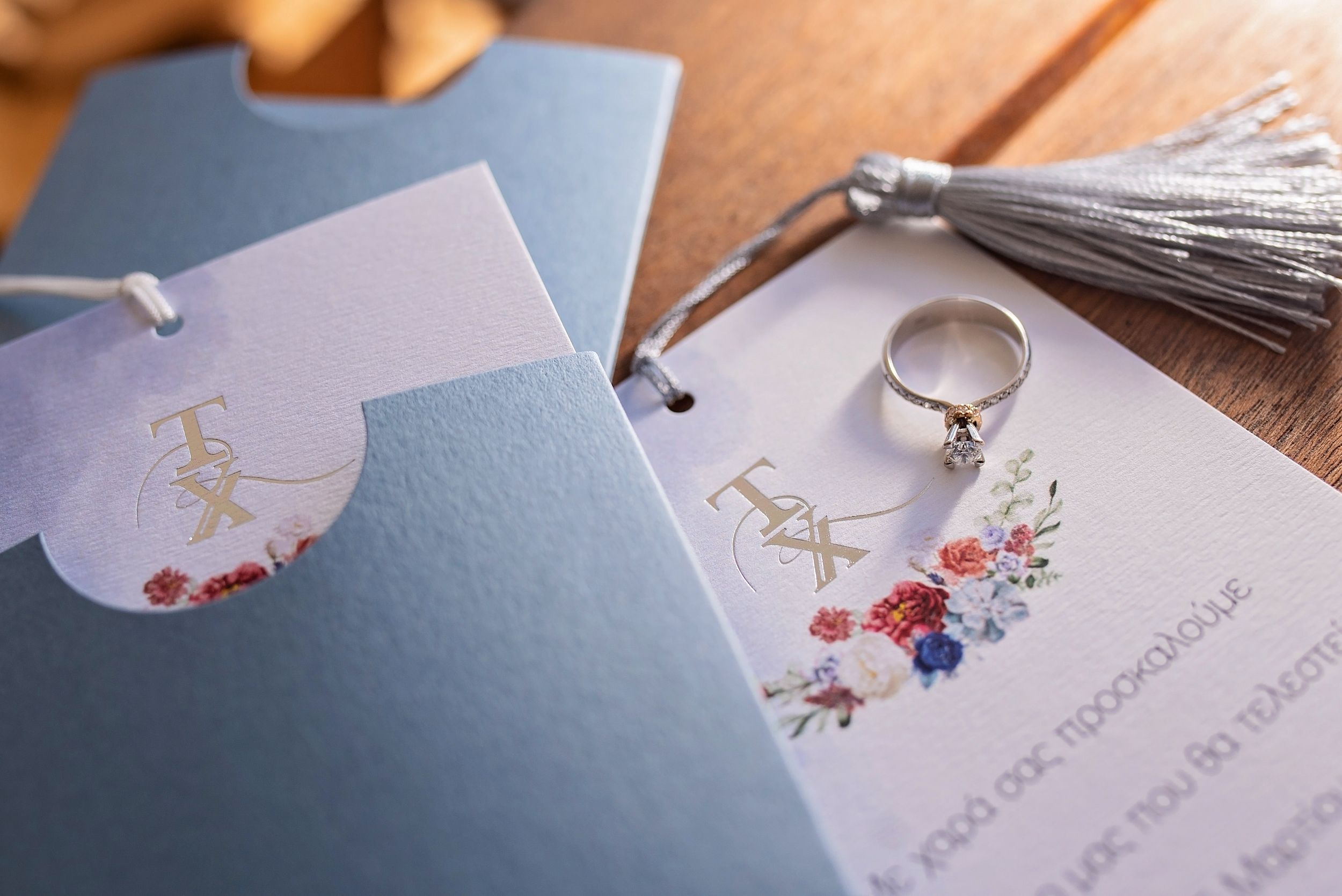 Wedding stationery with floral designs and an engagement ring displayed on blue paper.