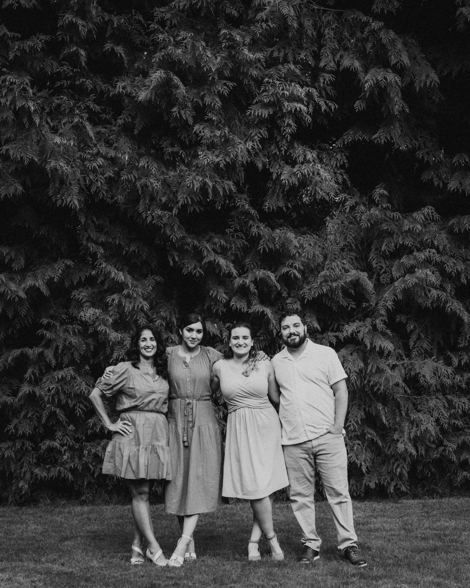 a black and white image of a family posing casually together in front of a large wall of dense manicured garden hedges.