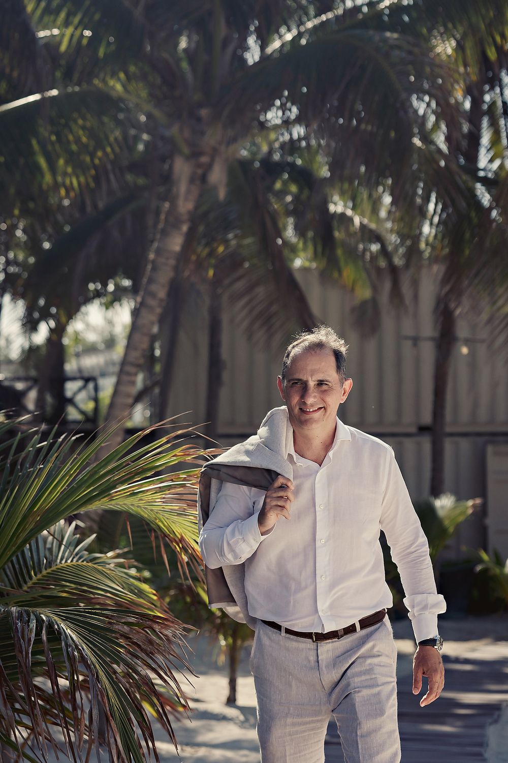 Person wearing crisp white attire walks along a tropical palm-lined path in bright sunlight.
