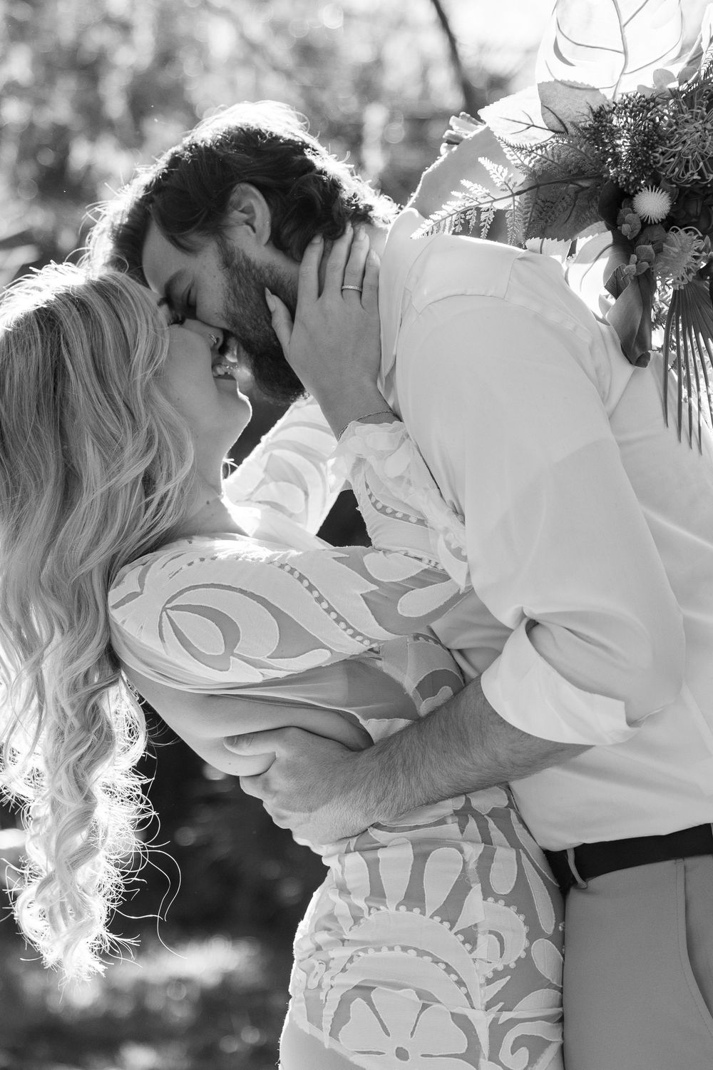 Black and white photo of a romantic embrace at a wedding, with the couple sharing an intimate moment in beautiful sunlight.