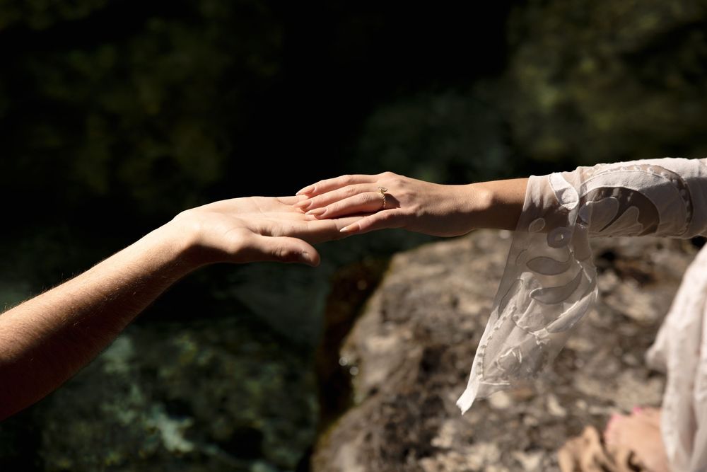 Two hands reaching towards each other against a dark blurred background, reminiscent of Michelangelo's Creation scene.