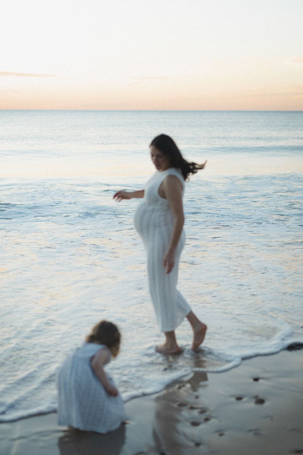 Two white-clad figures enjoy a peaceful moment on a serene beach at sunset with gentle waves lapping at their feet.