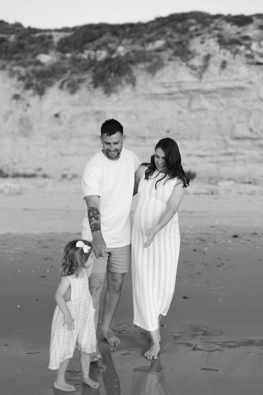 A family shares a tender moment together on a beach with cliffs in the background in black and white.