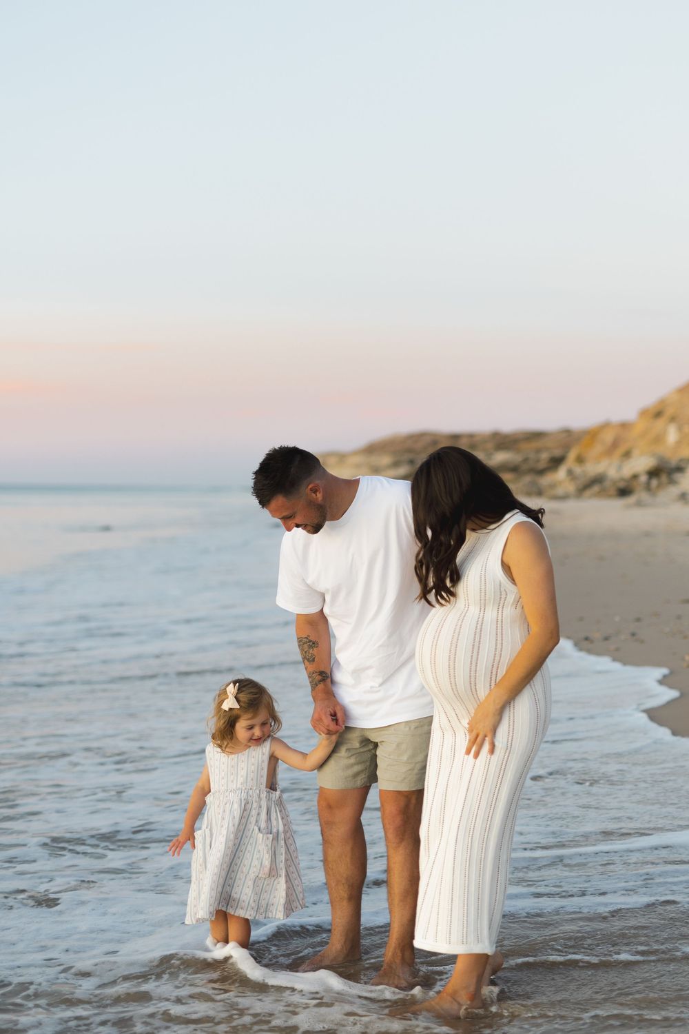 A family enjoys walking together along a peaceful beach at sunset while waves gently lap at their feet.