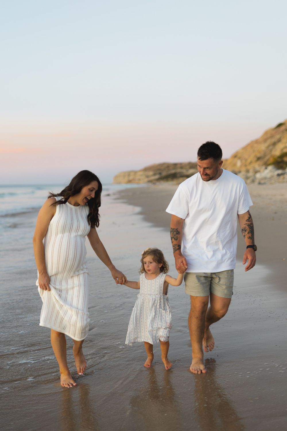 A family walks hand in hand along a sunset beach with coastal cliffs in the background.