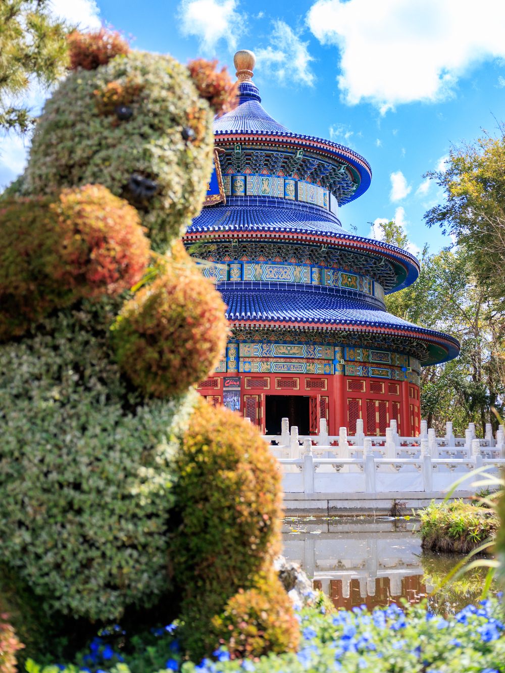 Temple of Heaven pagoda with traditional Chinese architecture surrounded by autumn foliage and blue flowers in Beijing.