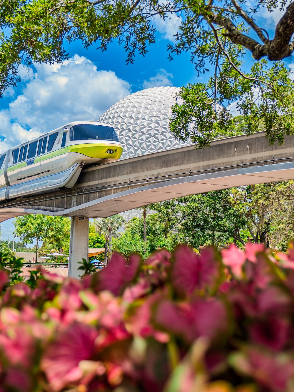 Monorail track curves past pink flowers with EPCOT's iconic Spaceship Earth sphere visible in the background.
