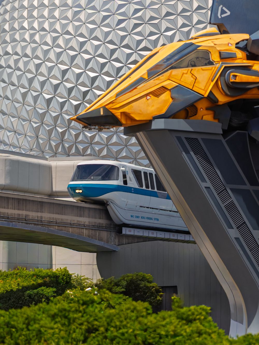 Yellow monorail train passes by the geometric facade of Epcot's Spaceship Earth.