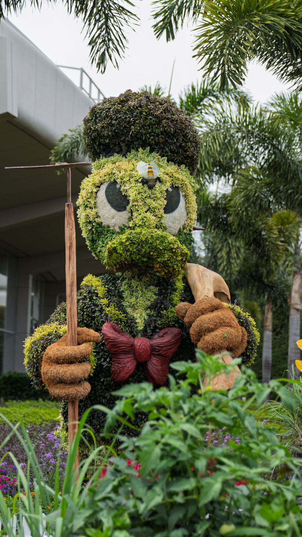 Topiary character with brown bow tie displayed in a lush garden setting.