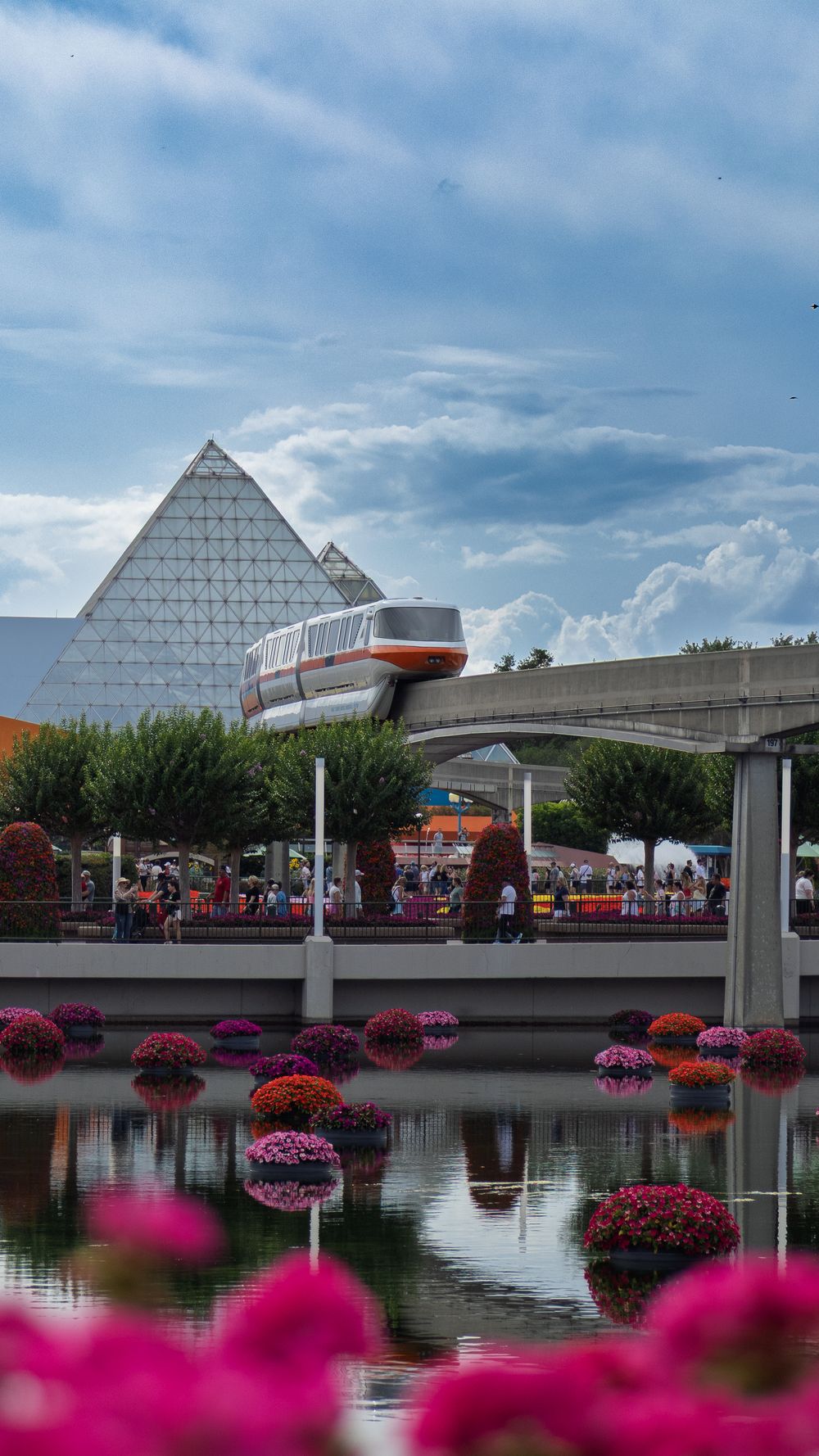 Modern pyramid-style building reflected in water with pink flowers in foreground.