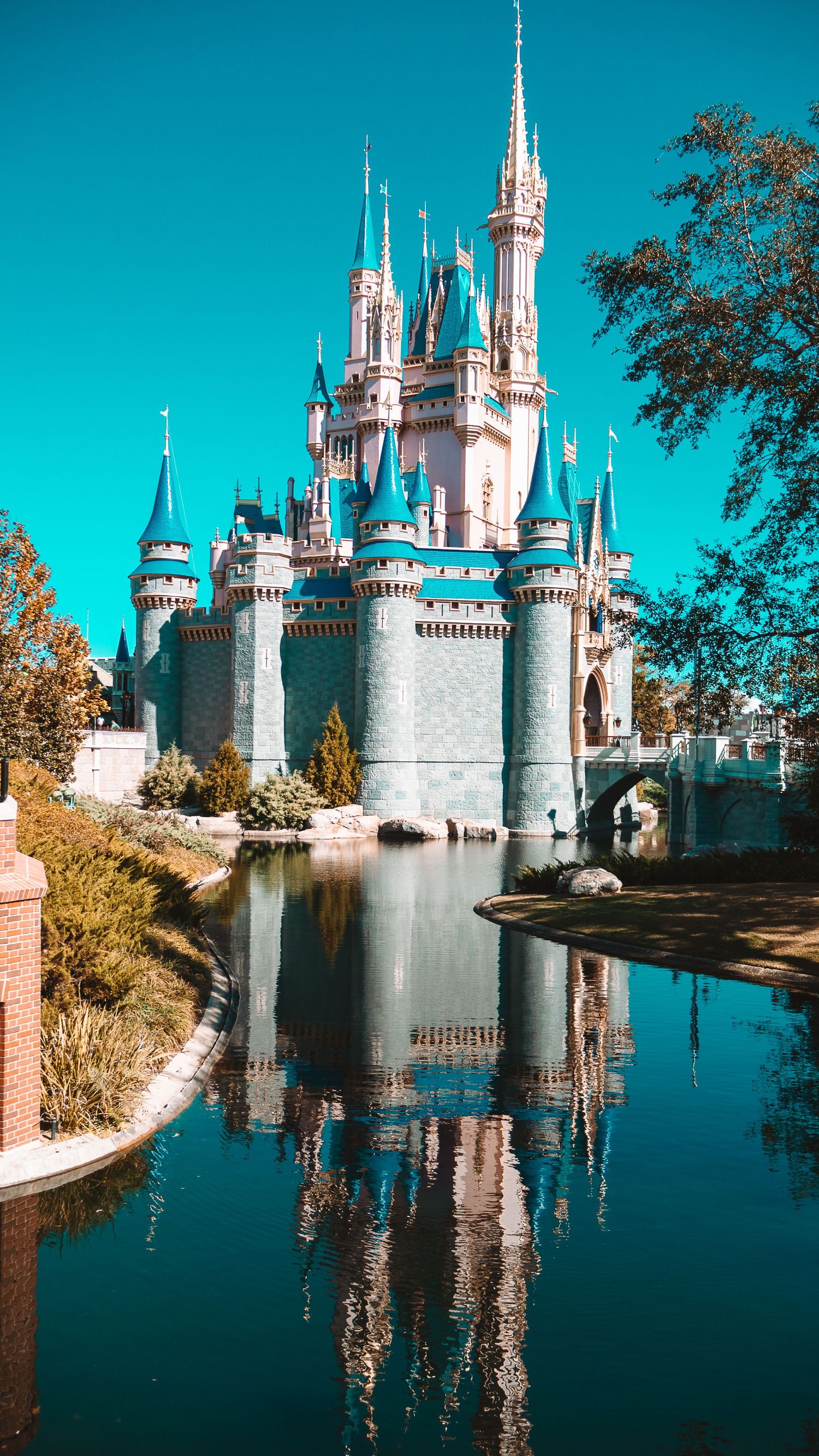 Cinderella Castle at Walt Disney World reflects in the moat waters against a bright turquoise sky.