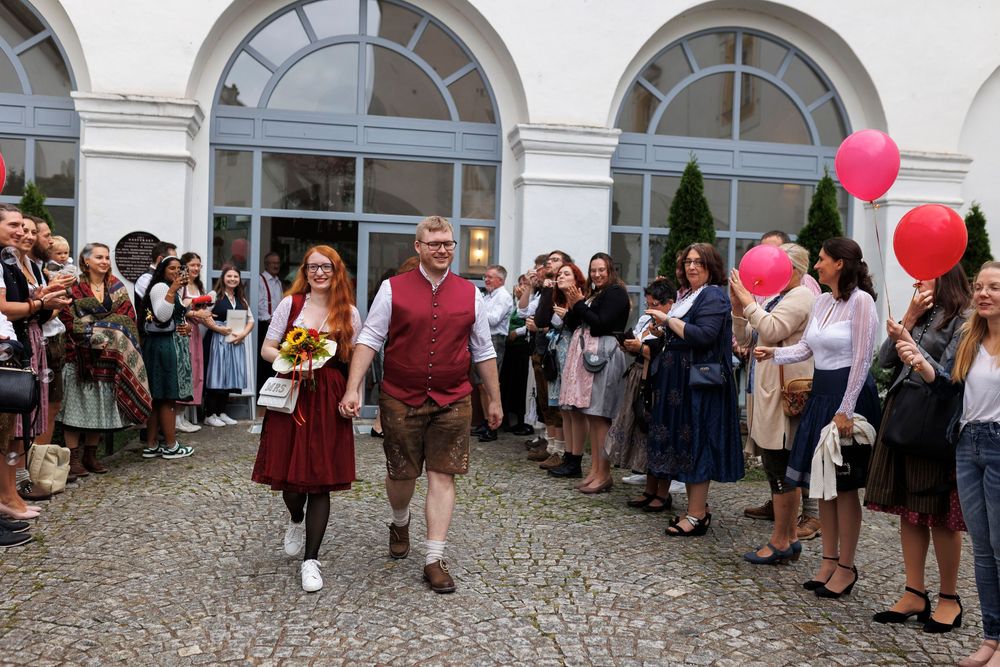 Wedding guests gather outside a white building with balloons and decorations.