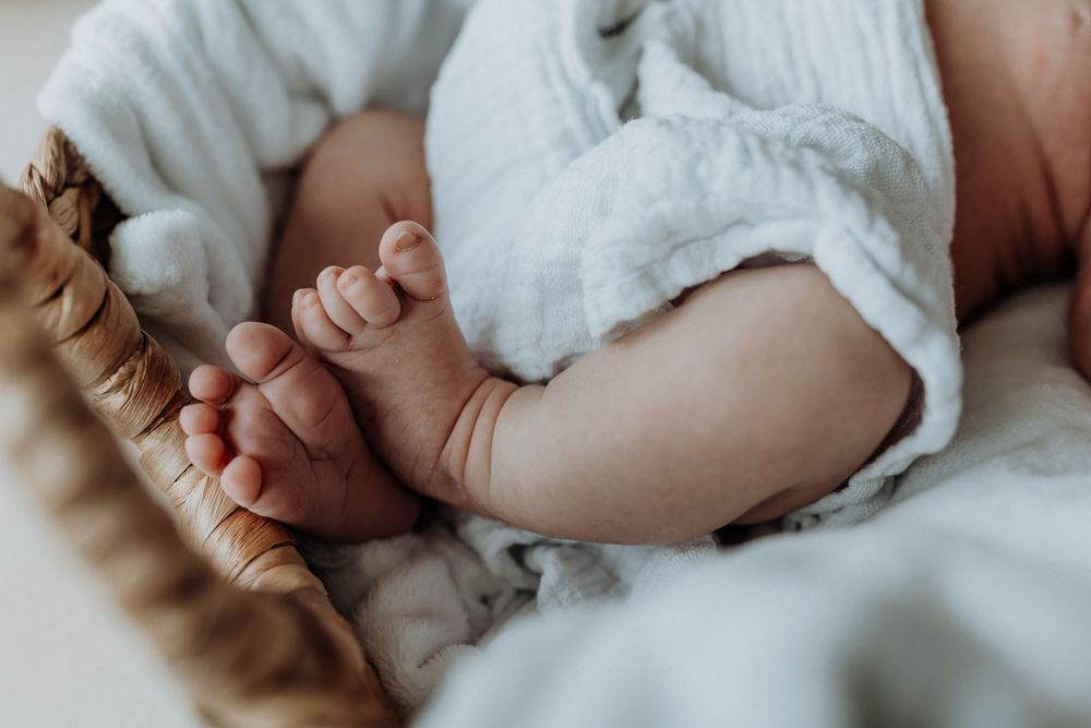Close-up view of tiny baby feet and hands wrapped in white fabric.