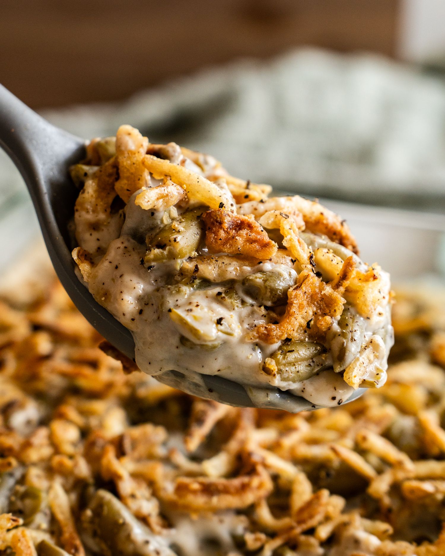 A creamy spoonful of green bean casserole topped with crispy fried onions being lifted from a glass dish.