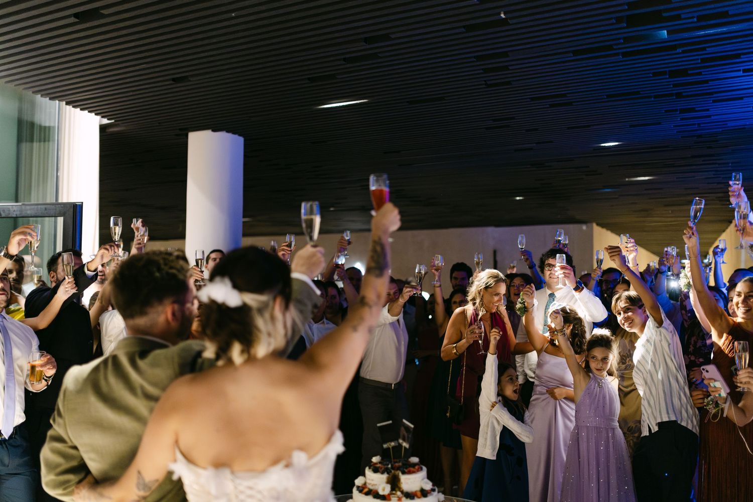 Wedding guests dance and celebrate on a dimly lit dance floor with blue lighting effects in the background.