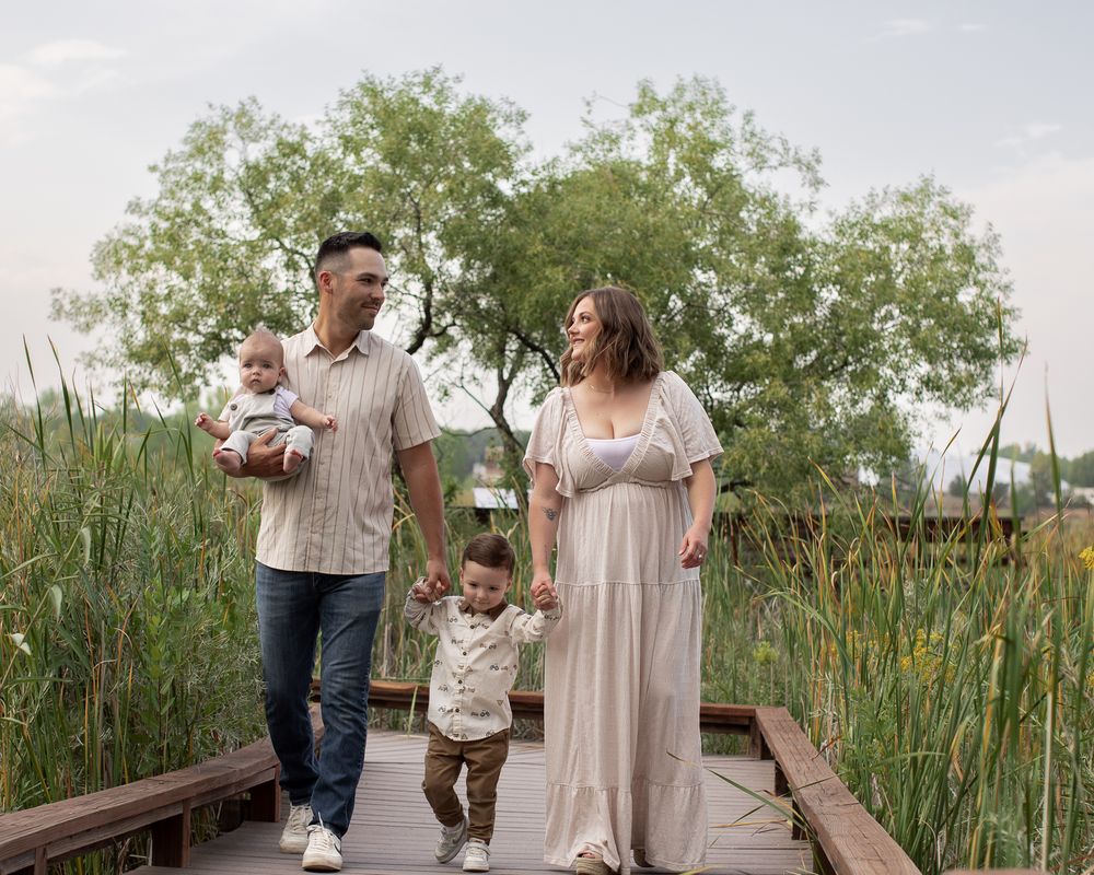 People strolling along a wooden walkway surrounded by lush green marsh grass and cattails in a nature preserve.