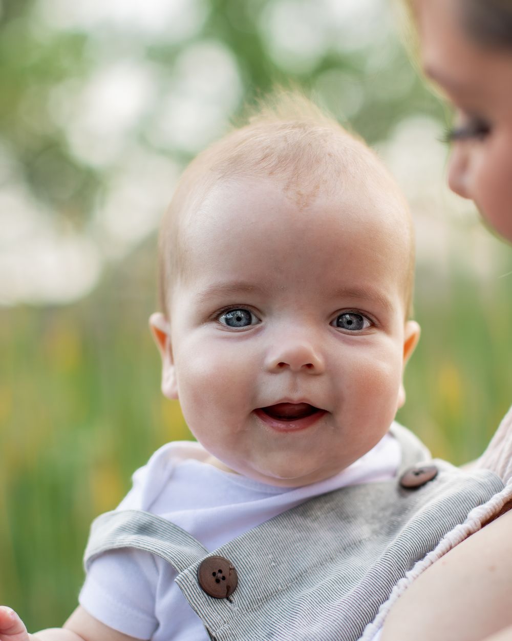Close up of baby with bright blue eyes and sweet smile wearing light colored outfit.