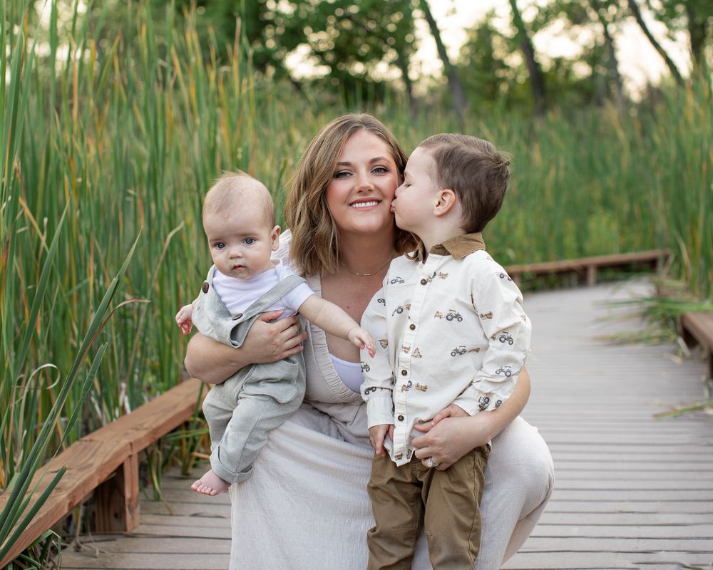 A joyful family moment captured on a wooden boardwalk surrounded by tall grass on a sunny day.