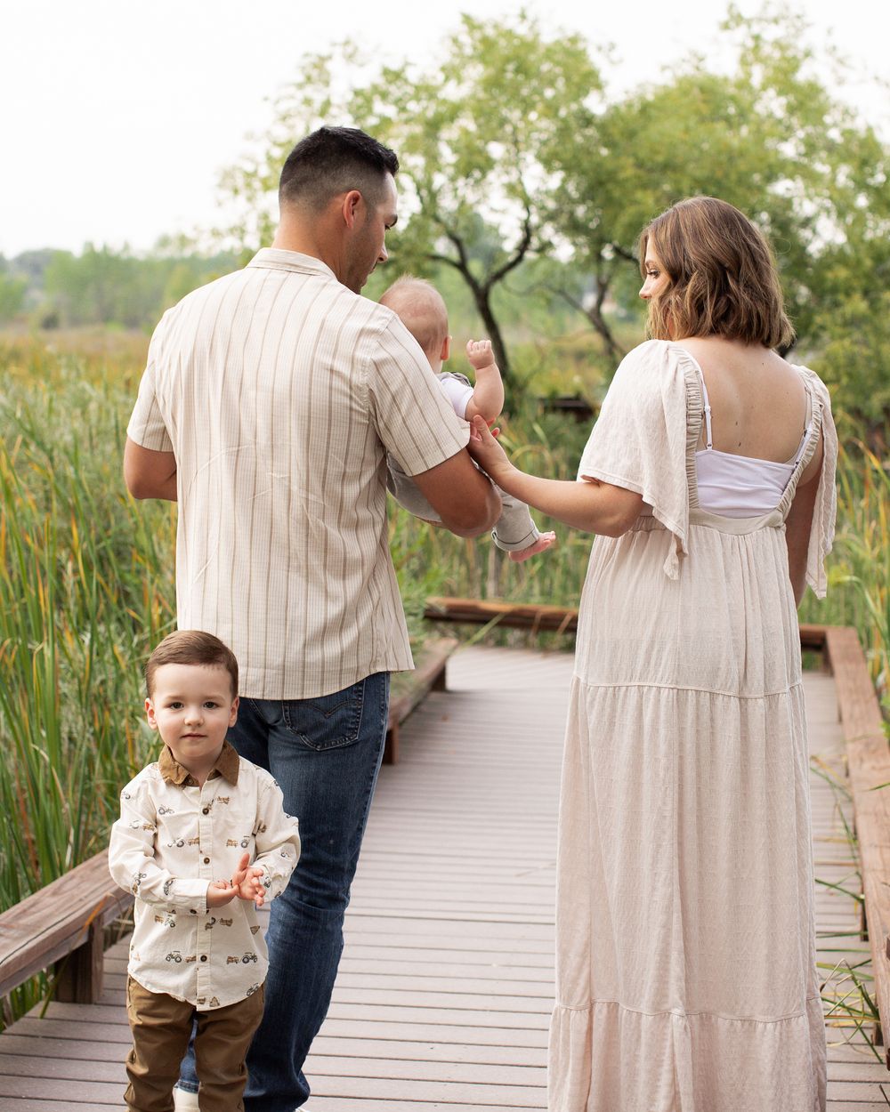 Family walking together on a wooden boardwalk through nature, holding hands and enjoying a sunny day.