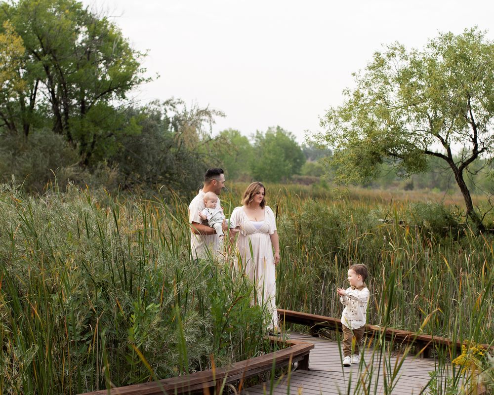 Family walking together on a wooden boardwalk path through tall reeds and natural wetlands on a summer day.
