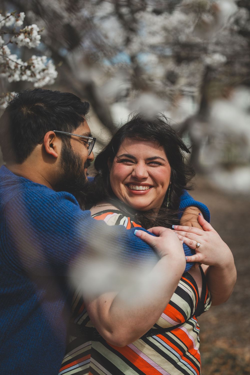 A couple shares tender moments while surrounded by delicate cherry blossoms in bloom during a spring proposal photoshoot.