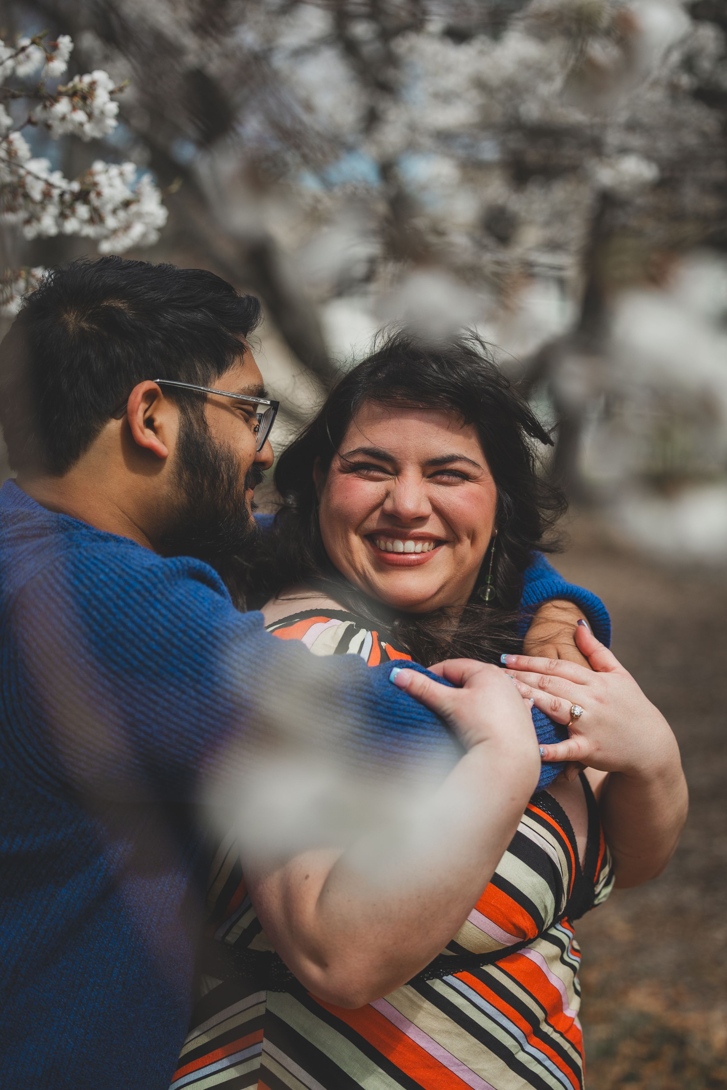 A couple shares tender moments while surrounded by delicate cherry blossoms in bloom during a spring proposal photoshoot.