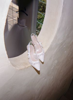 Elegant white bridal shoes with delicate lace details and bows displayed against a light background.